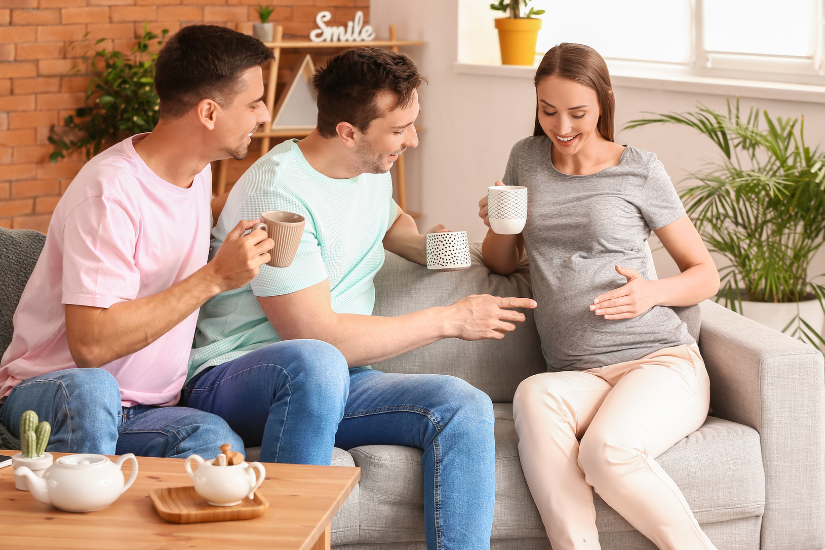 alt="gay couple looking at pregnant woman next to them."