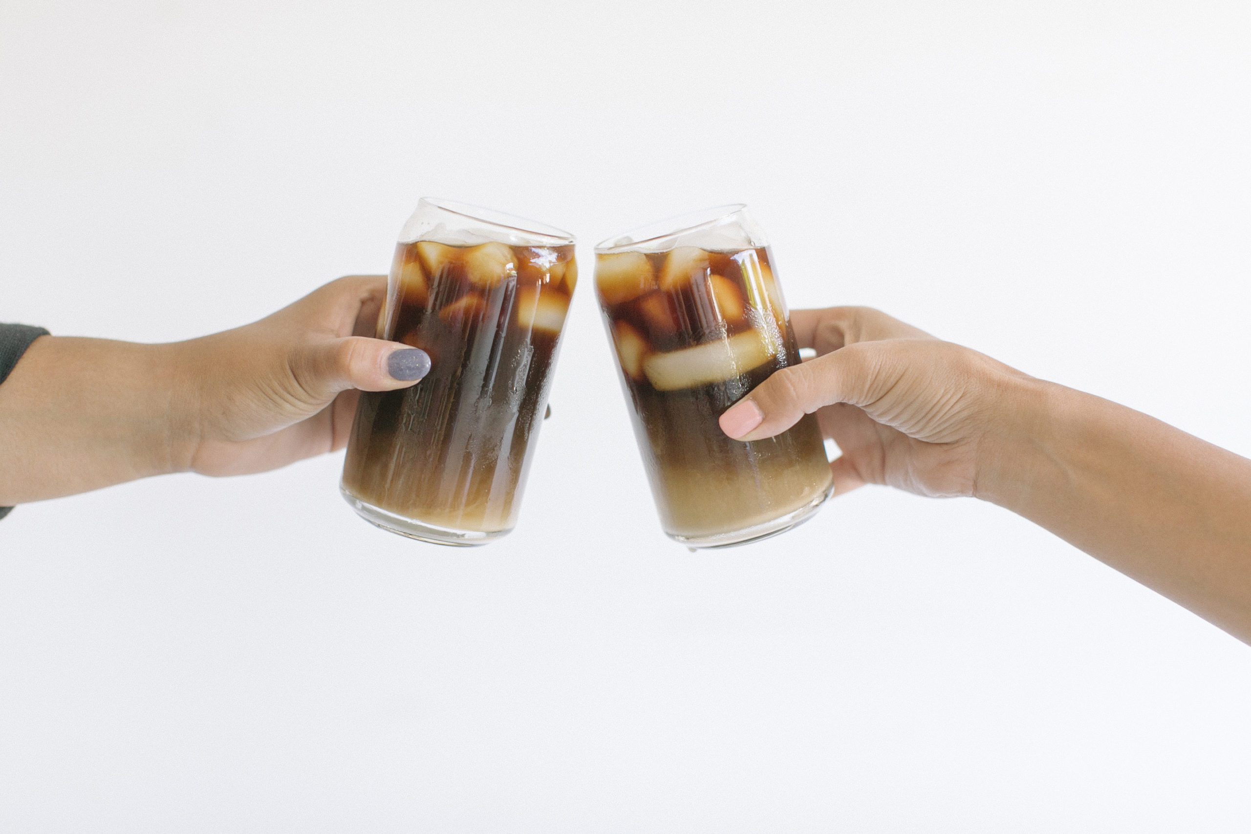 alt="white background, hands clinking glasses of iced coffee together, hybrid"