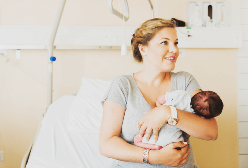 alt="young woman in hospital holding newborn baby"