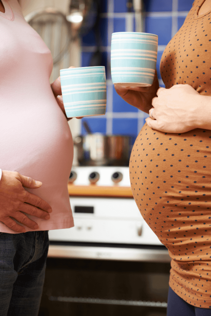 alt="close up of two pregnant women bellies, holding cups of coffee."