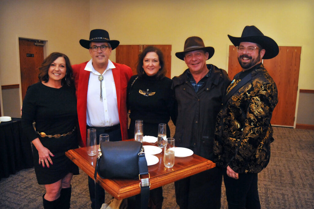 Group of five people in Western-themed attire posing at an indoor event.