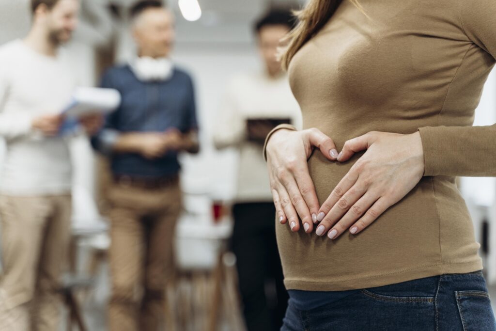 Pregnant businesswoman making a heart shape over her belly